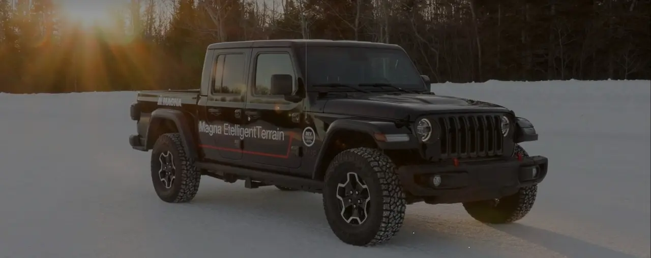 Black truck with Magna EtelligentTerrain branding parked on a snowy road with sunlight filtering through trees