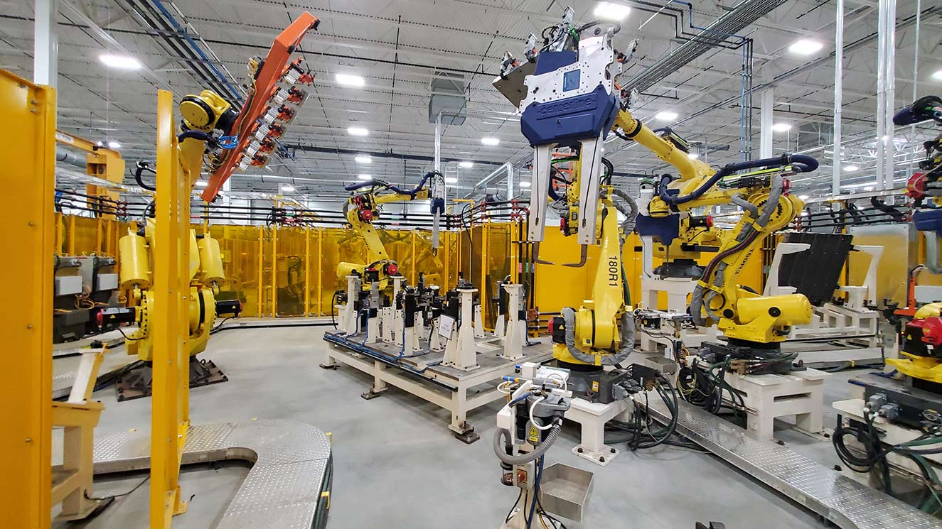 Person on a laptop at a vehicle manufacturing plant watching assembly line