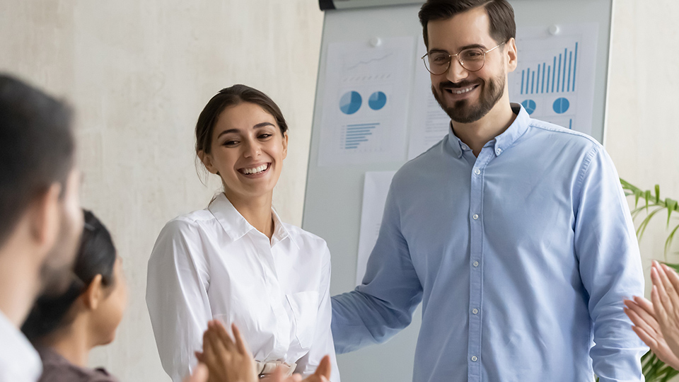 Smiling young businesswoman takes congratulations clap hands from diverse colleagues