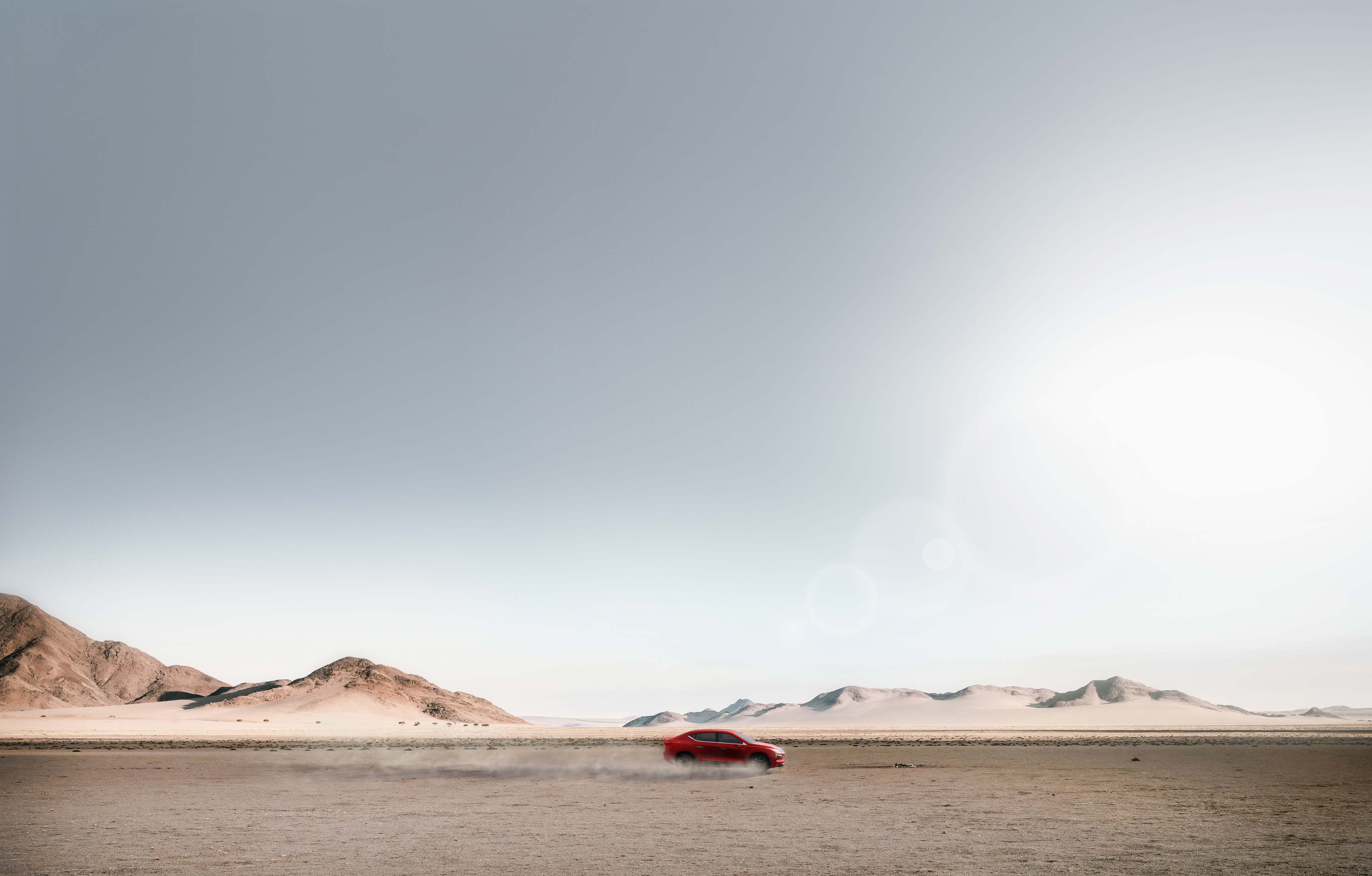 Red car driving across a wide desert landscape with mountains in the distance