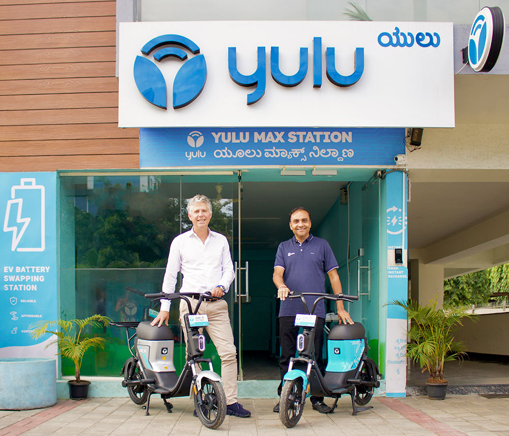 Two people standing in front of a building with electric two-wheelers.