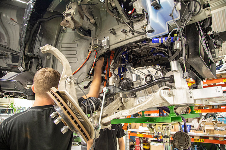 Engineers working on electric vehicle drivetrain and components under the chassis