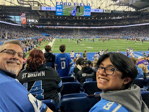 Jason Hegedus and other person smiling wearing Detroit Lions jersey sitting in the stands at Ford Field