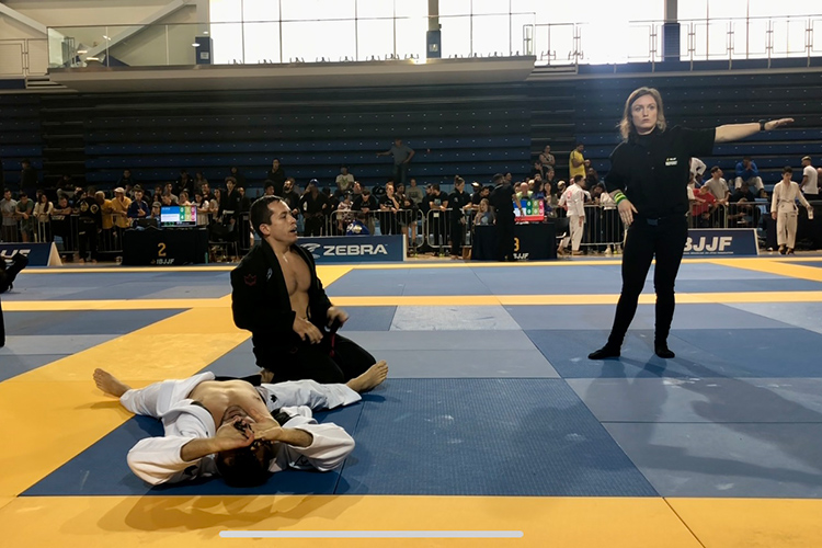 Two people participating in a Jiu-Jitsu match with a referee