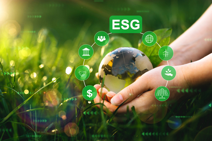 Hände halten einen Globus, umgeben von ESG-Symbolen, vor einem grasbewachsenen Hintergrund